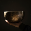 Hand holding a bronze singing bowl with engraved text against a dark background